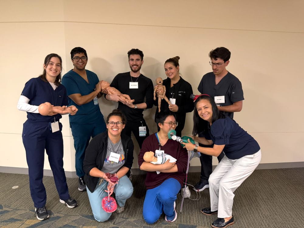 A group of healthcare workers from the ALSO training pose together, smiling and holding dolls used for training.