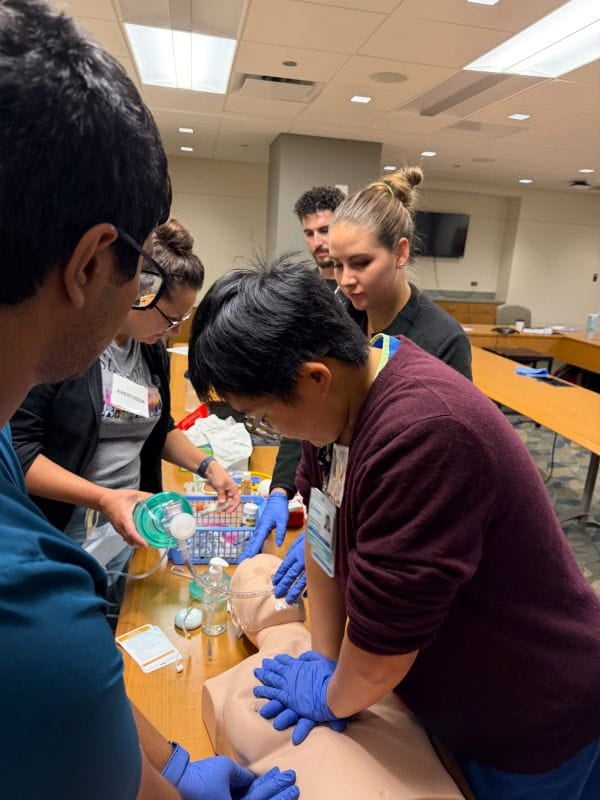 A group of people gather around a table, wearing gloves during CPR training