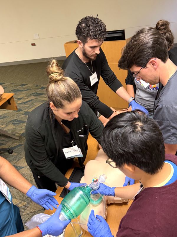 Residents wearing gloves practice intubation on a model.